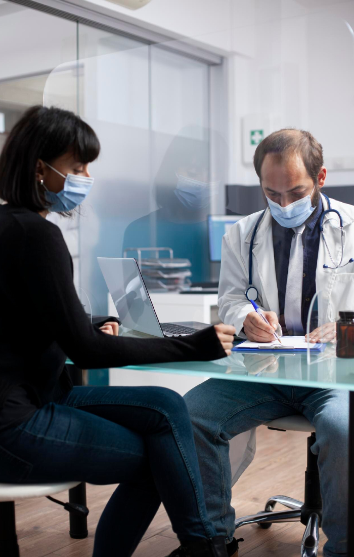 Doctor providing clinical supervision while consulting with a patient and completing medical documentation in a healthcare clinic.